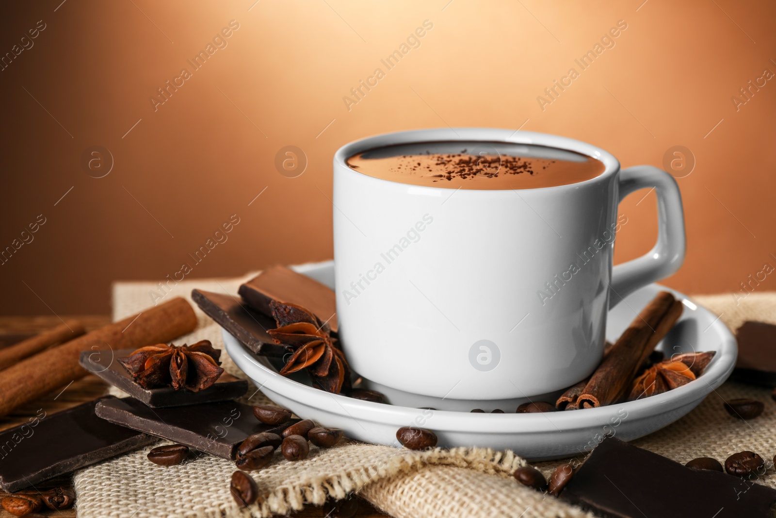 Photo of Cup of delicious hot chocolate, spices and coffee beans on table