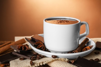 Cup of delicious hot chocolate, spices and coffee beans on table