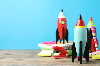 Photo of Bright toy rockets and school supplies on wooden table. Space for text