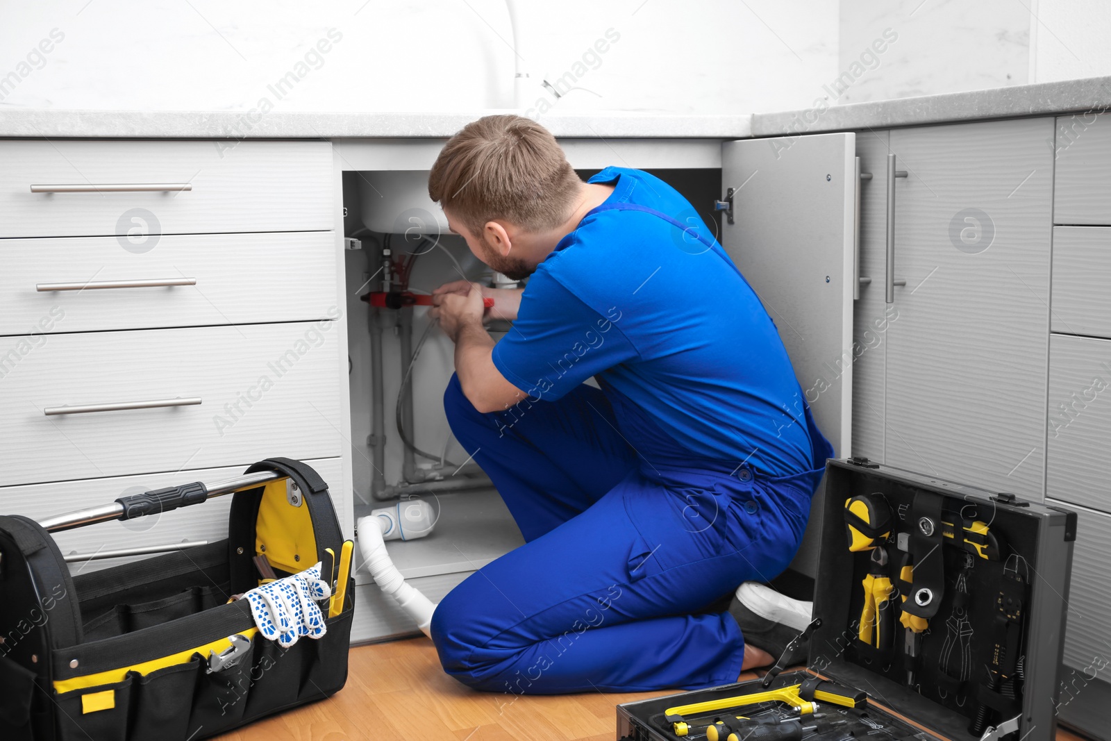 Photo of Professional plumber in uniform fixing kitchen sink