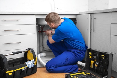 Professional plumber in uniform fixing kitchen sink