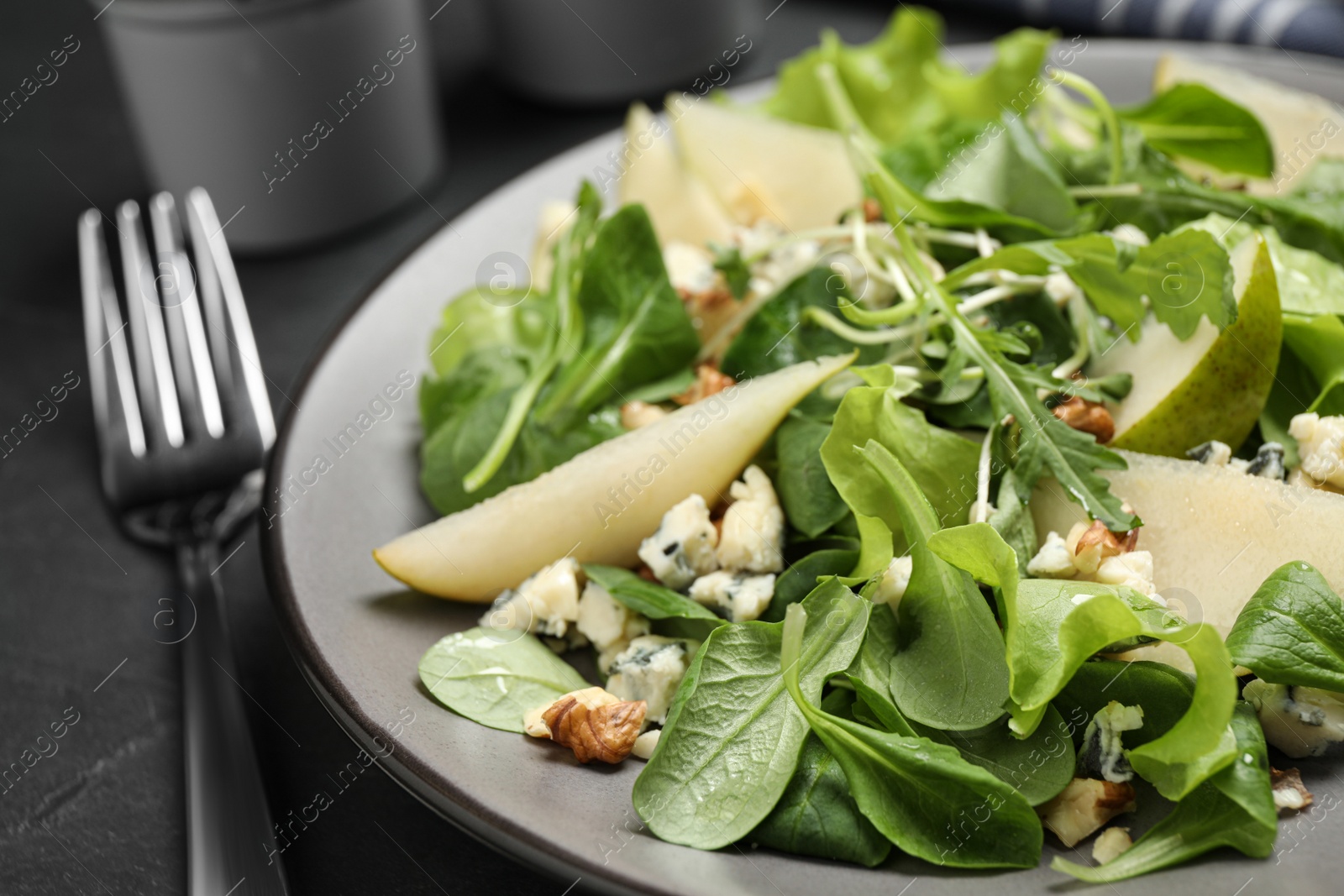 Photo of Tasty salad with pear slices and fork on black table, closeup