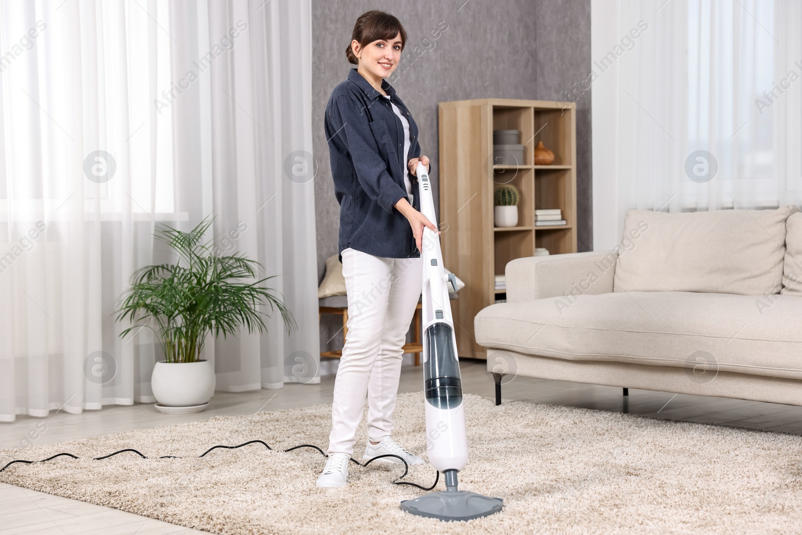 Photo of Happy young housewife vacuuming carpet at home