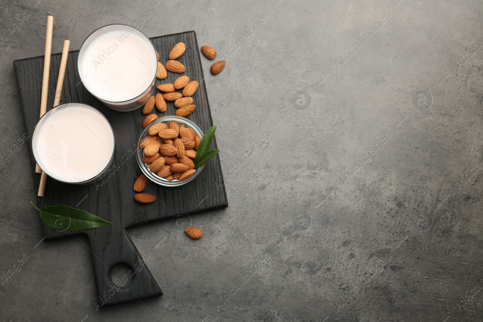 Photo of Glasses of almond milk and almonds on grey table, top view. Space for text