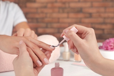 Manicurist applying polish on client's nails at table, closeup. Spa treatment