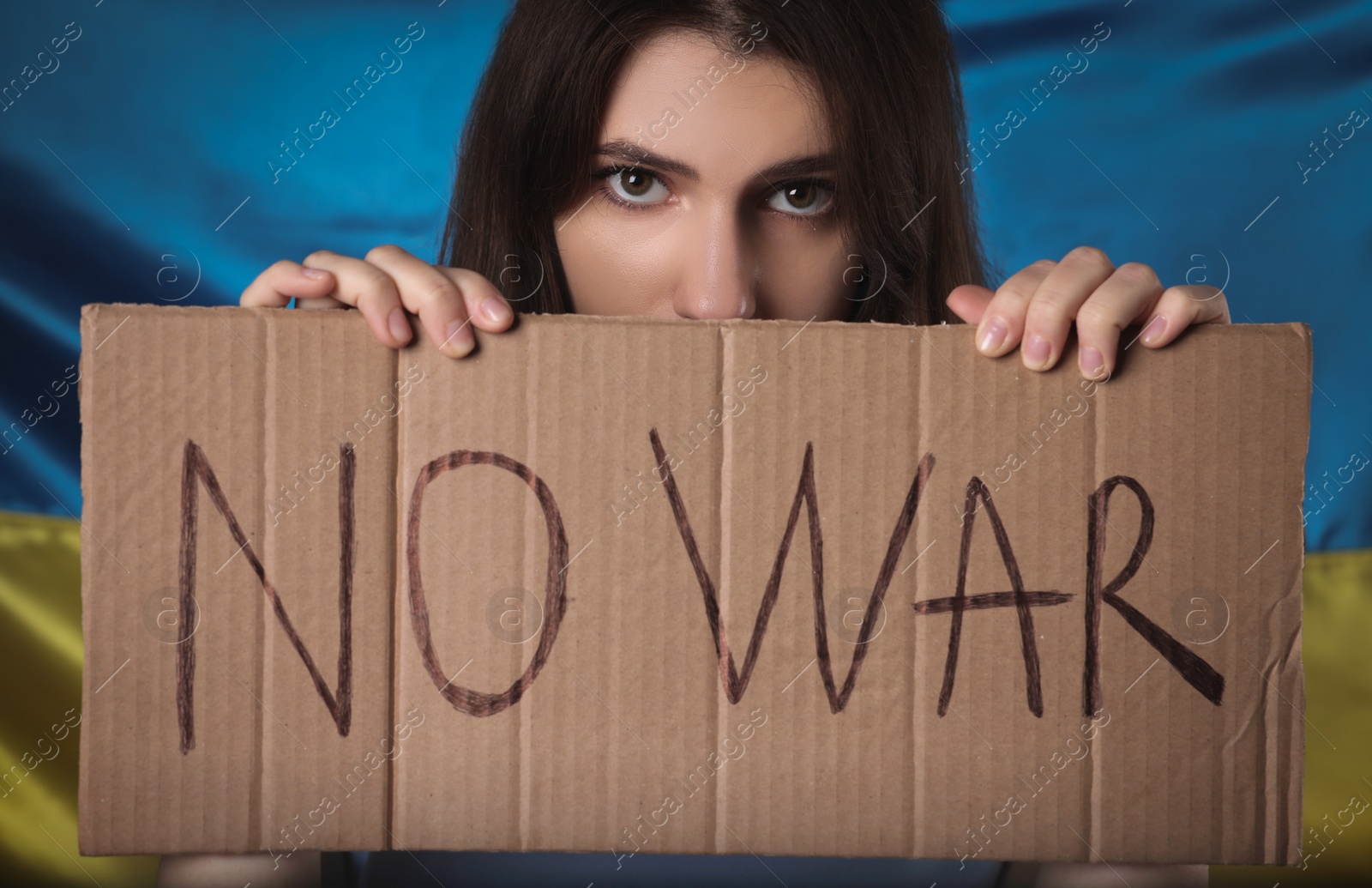 Photo of Sad woman holding poster with words No War near Ukrainian flag, closeup