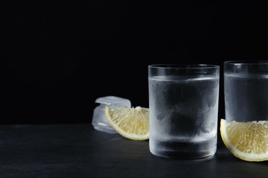 Photo of Shot glasses of vodka with lemon slices and ice on black background. Space for text