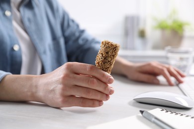 Photo of Woman holding tasty granola bar at light table in office, closeup