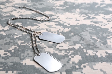 Photo of Metal military ID tags on camouflage background. Space for text