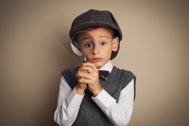 Little boy with magnifying glass playing detective on beige background