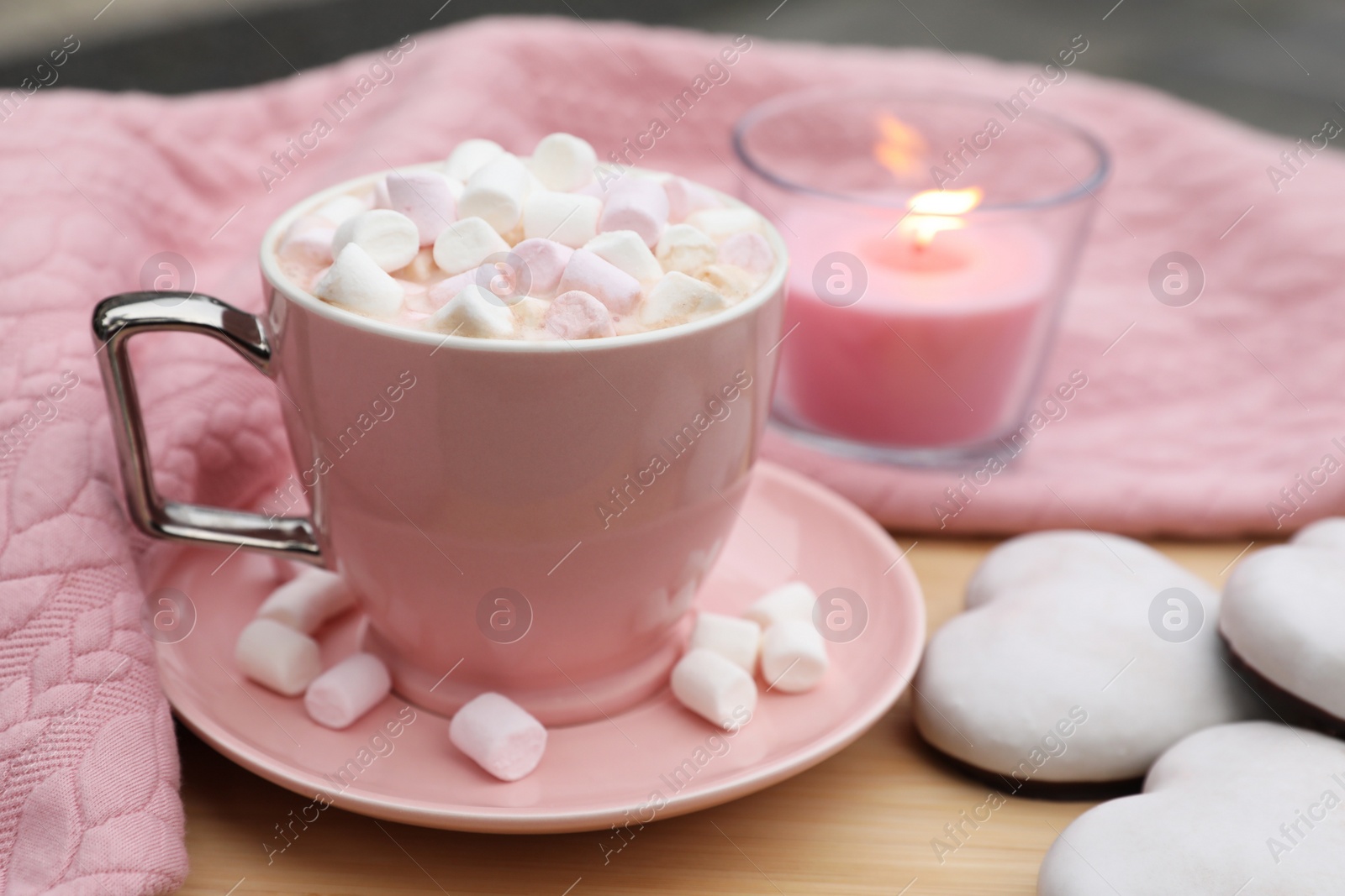 Photo of Cup of tasty cocoa with marshmallows, pink sweater, cookies and burning candle on wooden table