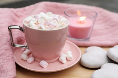 Cup of tasty cocoa with marshmallows, pink sweater, cookies and burning candle on wooden table
