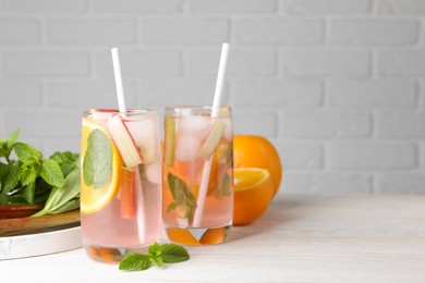 Tasty rhubarb cocktail with orange on white wooden table, space for text
