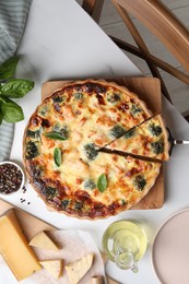 Photo of Taking piece of delicious homemade quiche and ingredients on white table, flat lay