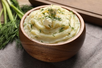 Photo of Bowl of delicious mashed potato with dill and butter on grey tablecloth, closeup