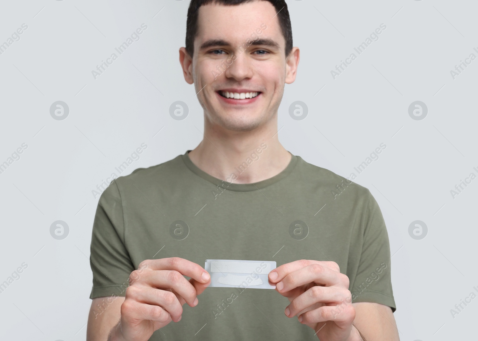 Photo of Young man with whitening strips on light grey background