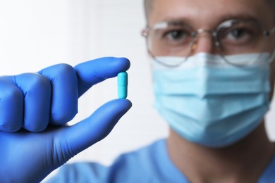 Doctor holding pill on light background, selective focus. Space for text