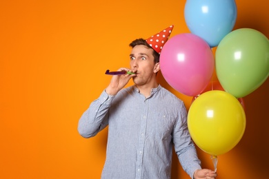 Young man with bright balloons and party blower on color background. Birthday celebration