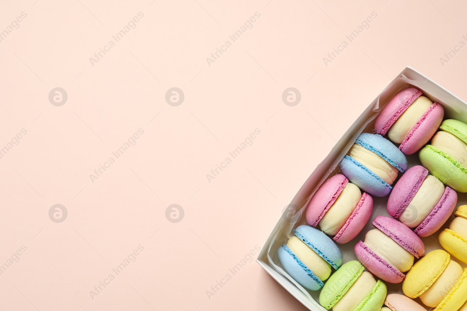 Photo of Many delicious colorful macarons in box on pink background, top view. Space for text