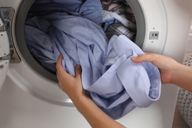 Photo of Woman taking laundry out of washing machine indoors, closeup
