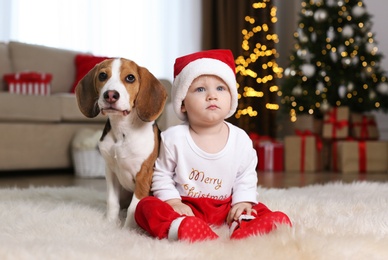 Baby in Santa hat and cute Beagle dog at home against blurred Christmas lights