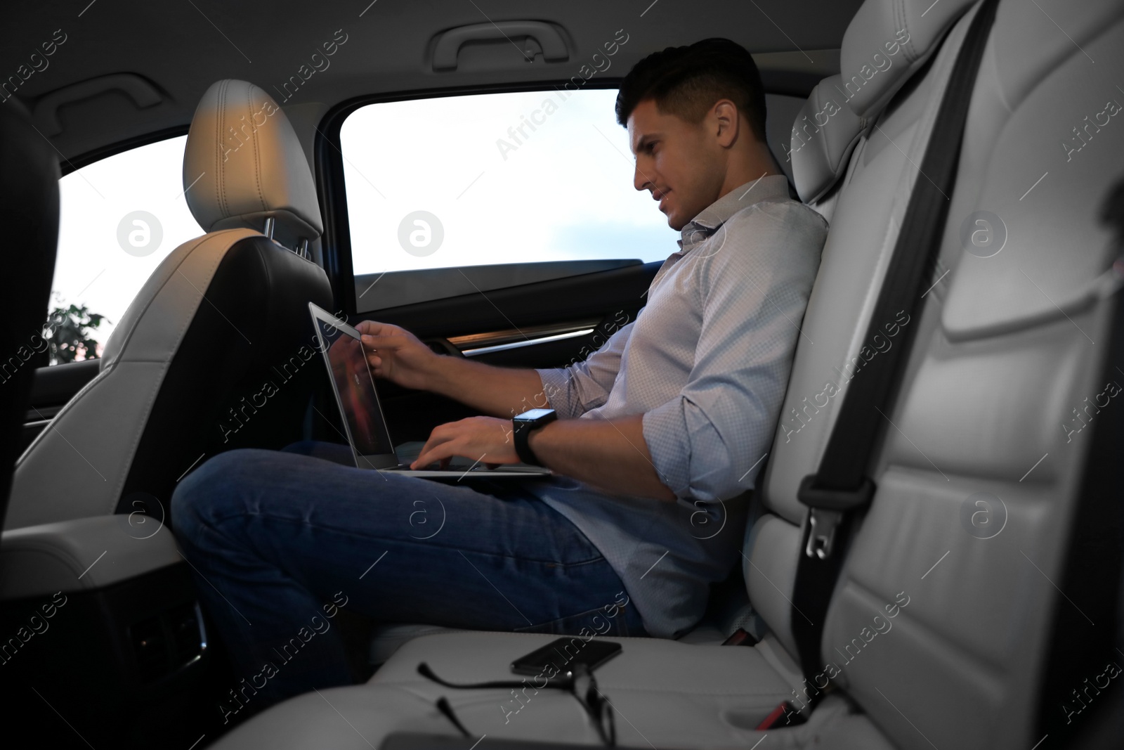 Photo of Handsome man working with laptop on backseat of modern car