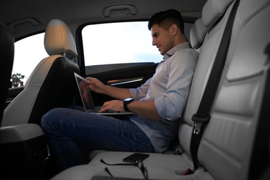 Handsome man working with laptop on backseat of modern car