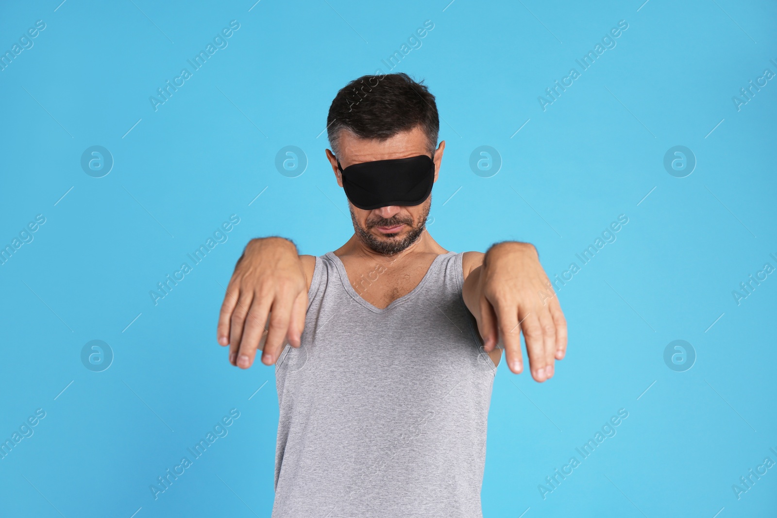 Photo of Man with eye mask in sleepwalking state on light blue background