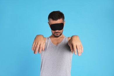 Man with eye mask in sleepwalking state on light blue background