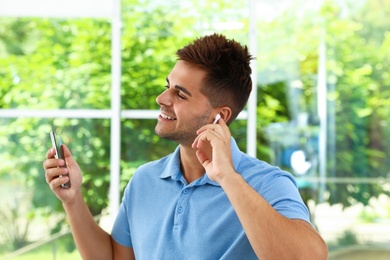 Photo of Happy young man with smartphone listening to music through wireless earphones indoors