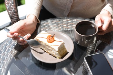 Photo of Woman drinking coffee and eating tasty dessert at glass table outdoors, closeup