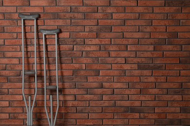 Photo of Pair of axillary crutches near red brick wall. Space for text