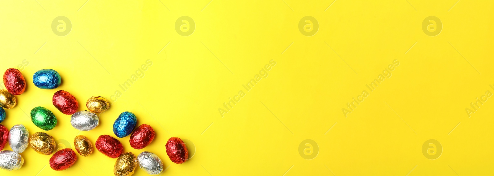 Image of Chocolate eggs wrapped in colorful foil on yellow background, flat lay with space for text. Banner design