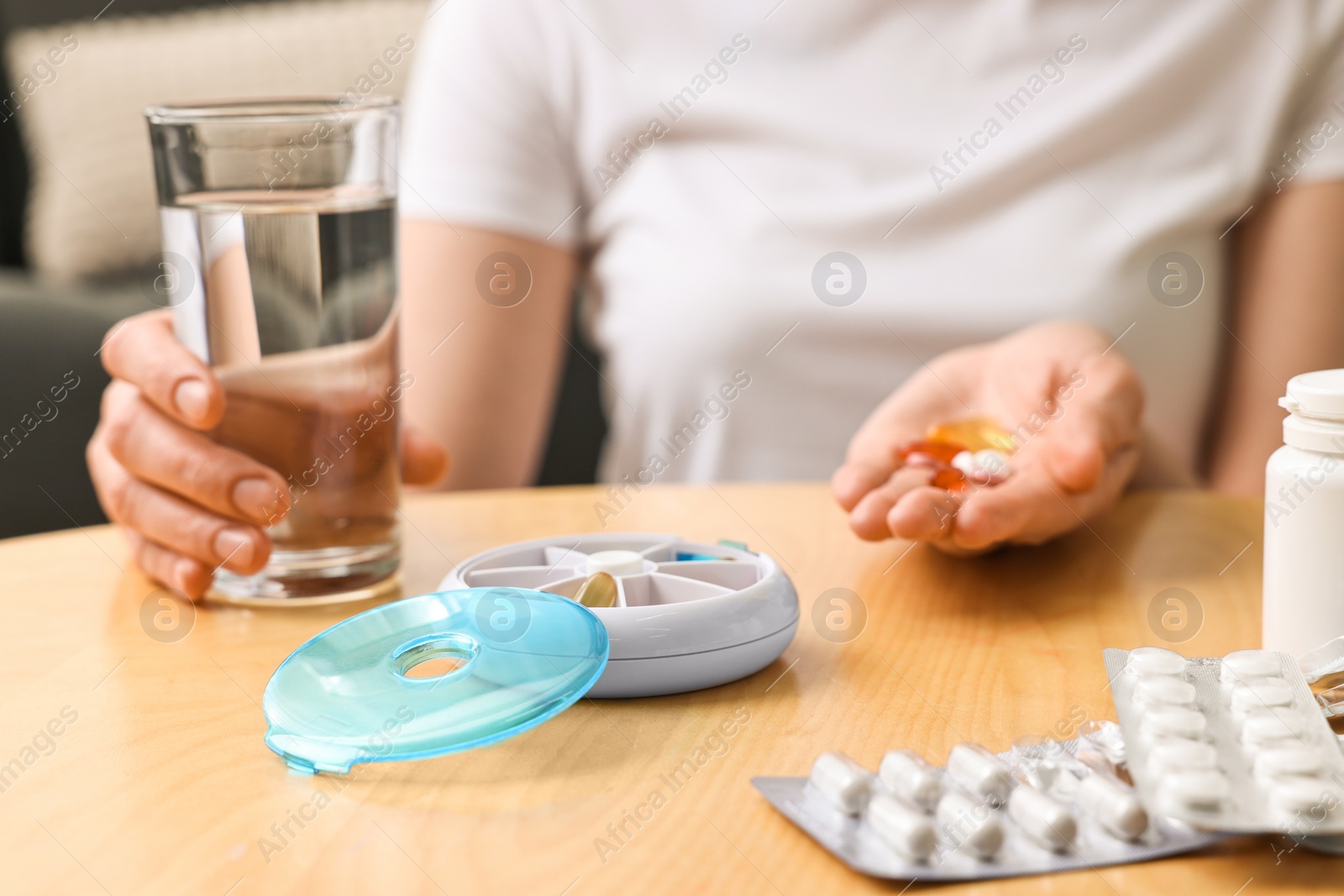 Photo of Woman with pills, organizer and glass of water at light wooden table, selective focus