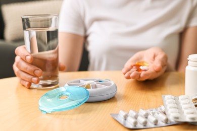 Woman with pills, organizer and glass of water at light wooden table, selective focus