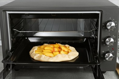 Open electric oven with uncooked pie on table in kitchen