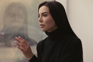 Photo of Depressed woman near window on rainy day