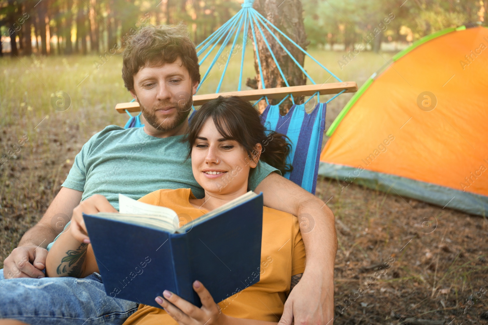 Photo of Lovely couple with book resting in comfortable hammock outdoors