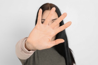 Young woman making stop gesture against white background, focus on hand