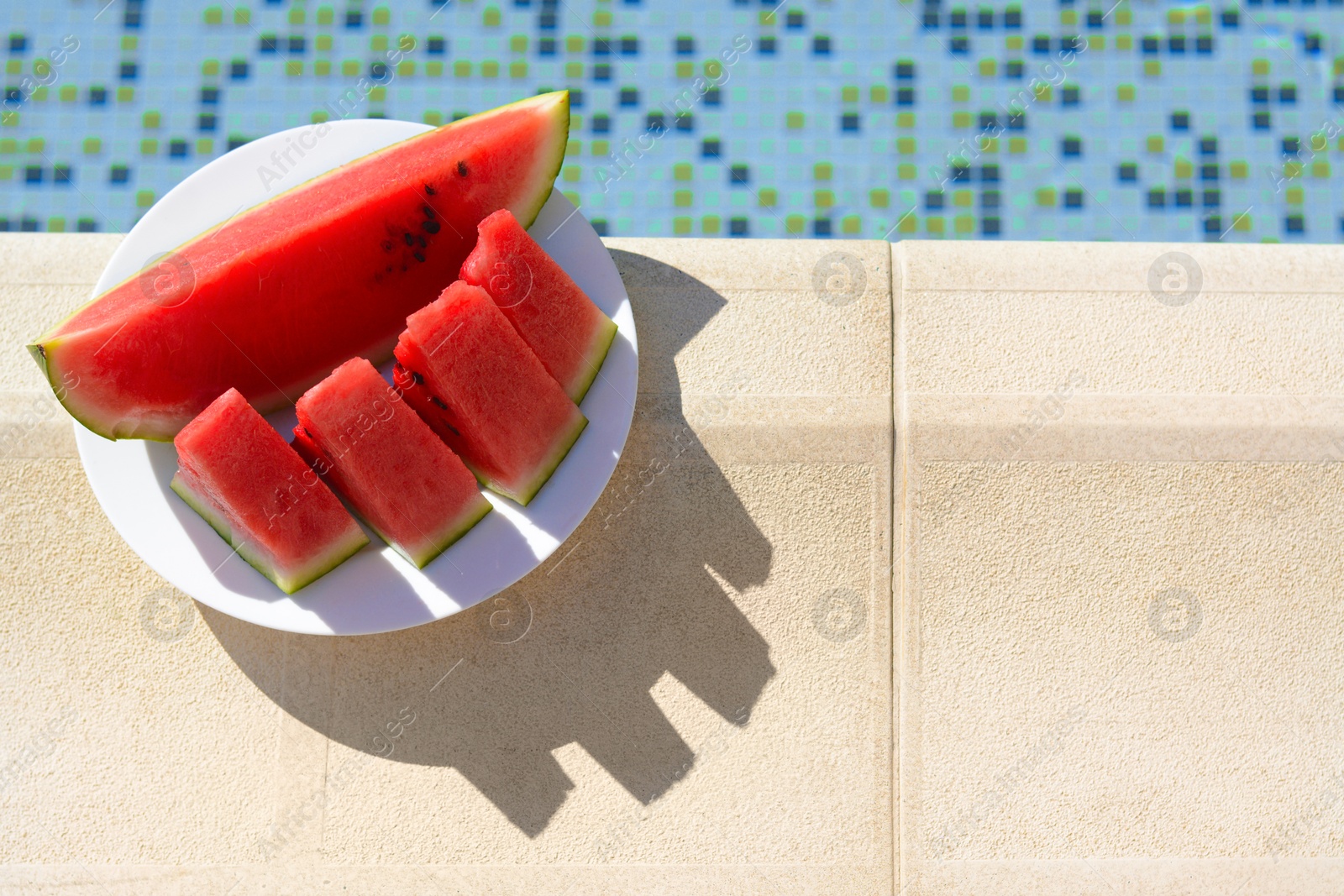 Photo of Slices of watermelon on white plate near swimming pool outdoors, top view. Space for text