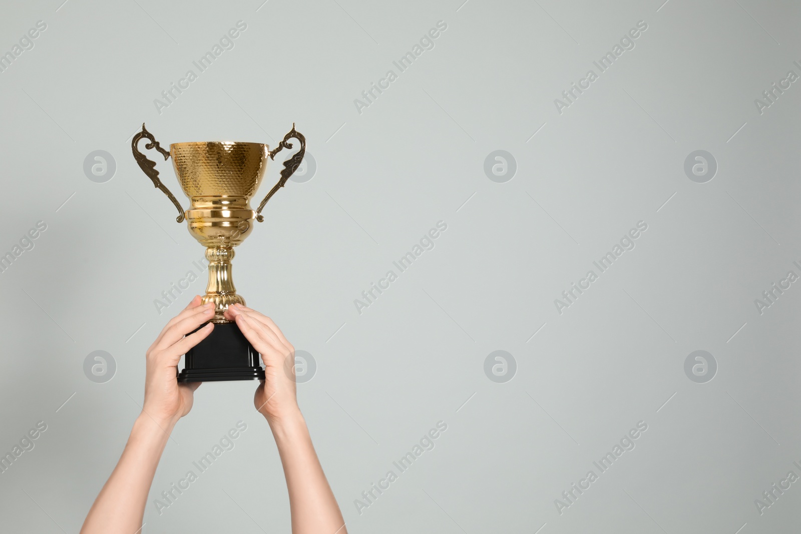 Photo of Man holding gold trophy cup on light grey background, closeup. Space for text