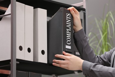 Woman taking folder with Complaints label in office, closeup