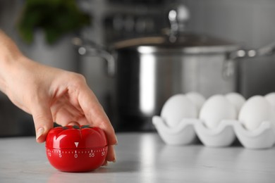 Photo of Woman winding up kitchen timer in shape of tomato at white table indoors, closeup. Space for text