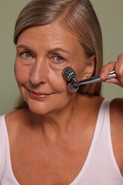 Photo of Woman massaging her face with metal roller on green background