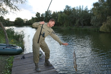 Man with rod and catch fishing on wooden pier at riverside. Recreational activity