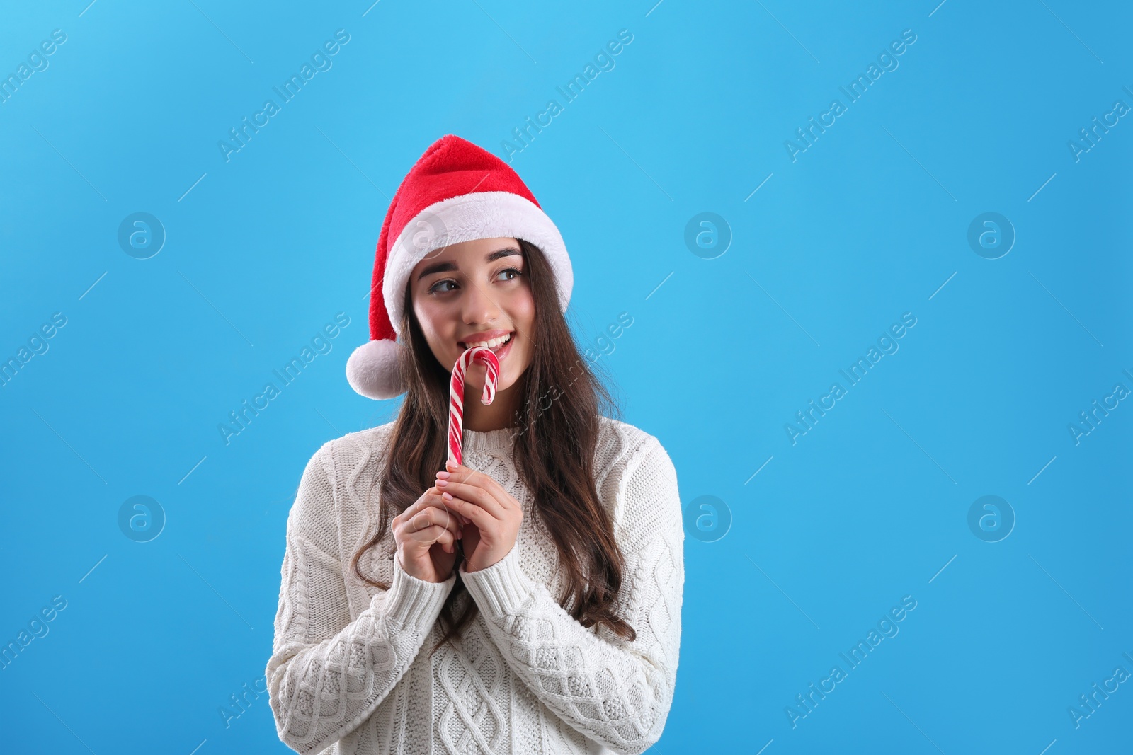 Photo of Beautiful woman in Santa Claus hat holding candy cane on light blue background