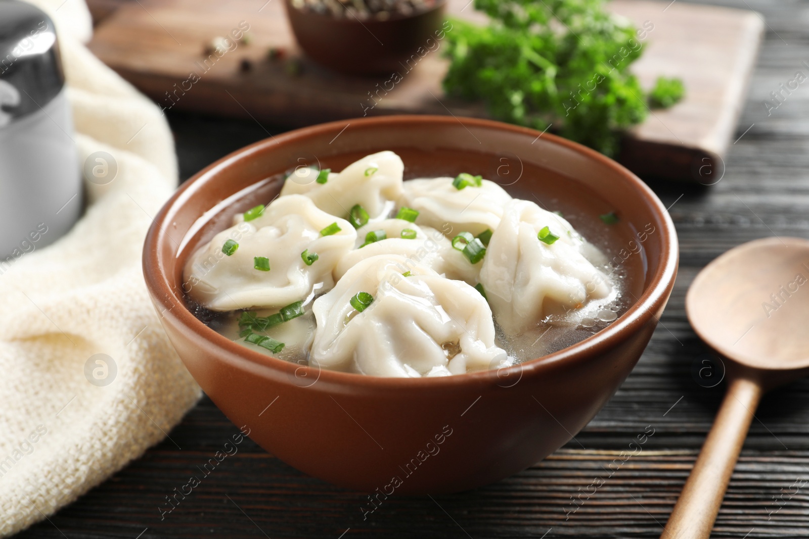 Photo of Bowl of tasty dumplings in broth and spoon on wooden table