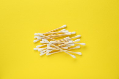 Heap of wooden cotton buds on yellow background, flat lay