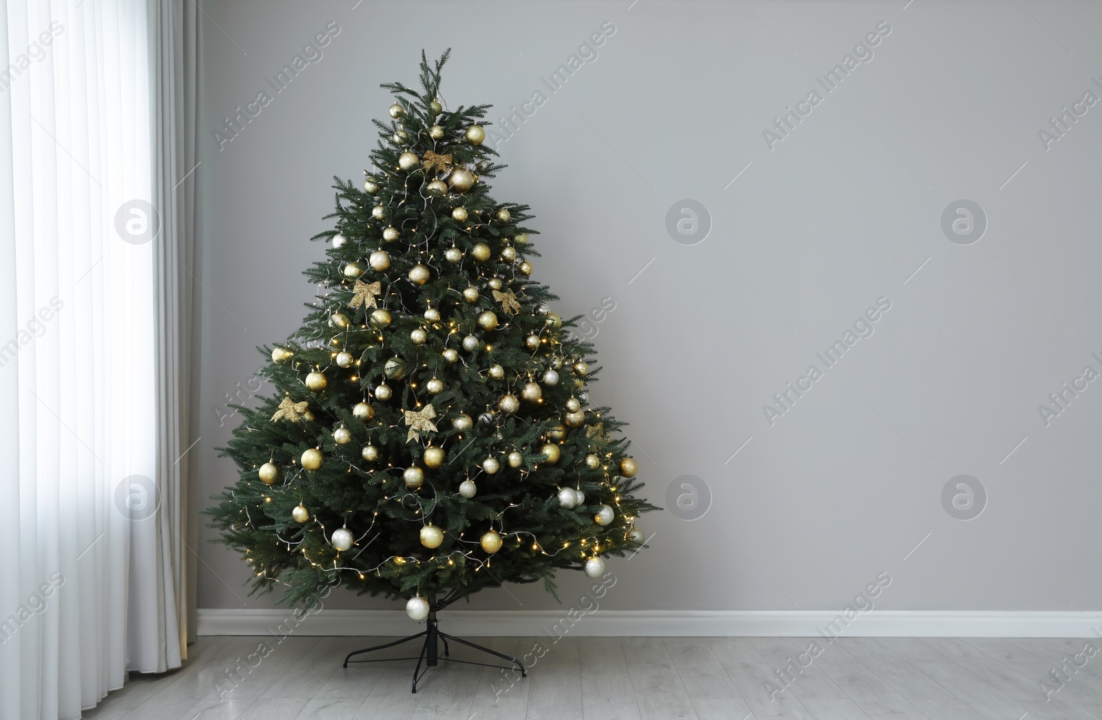 Photo of Beautifully decorated Christmas tree near grey wall indoors, space for text