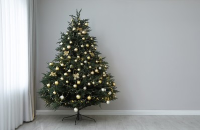 Photo of Beautifully decorated Christmas tree near grey wall indoors, space for text